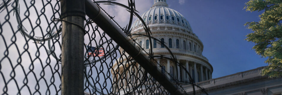A view of the U.S. Capitol Building at an angle behind razor wire fencing with clouds in the background.