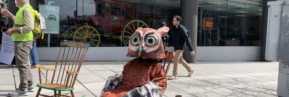 An actor dressed as an owl from our street theater skit sits in a rocking chair outside a Wells Fargo