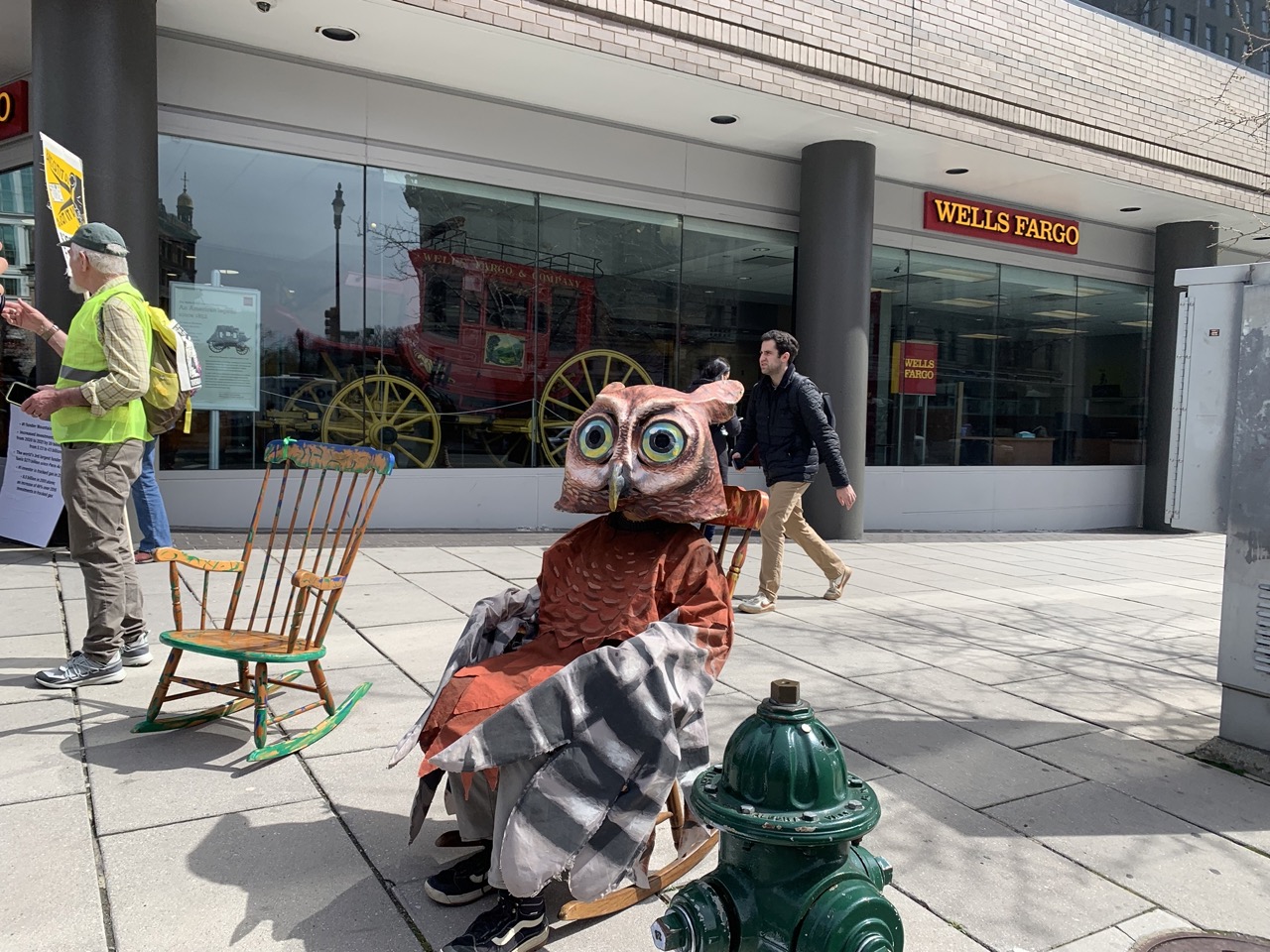 An actor dressed as an owl from our street theater skit sits in a rocking chair outside a Wells Fargo